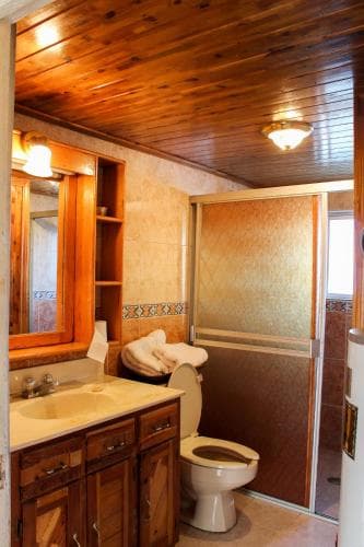 A cozy cabin-style bathroom with wooden ceilings, warm lighting, tiled walls, and rustic fixtures offers a serene retreat for travelers seeking comfort in nature.