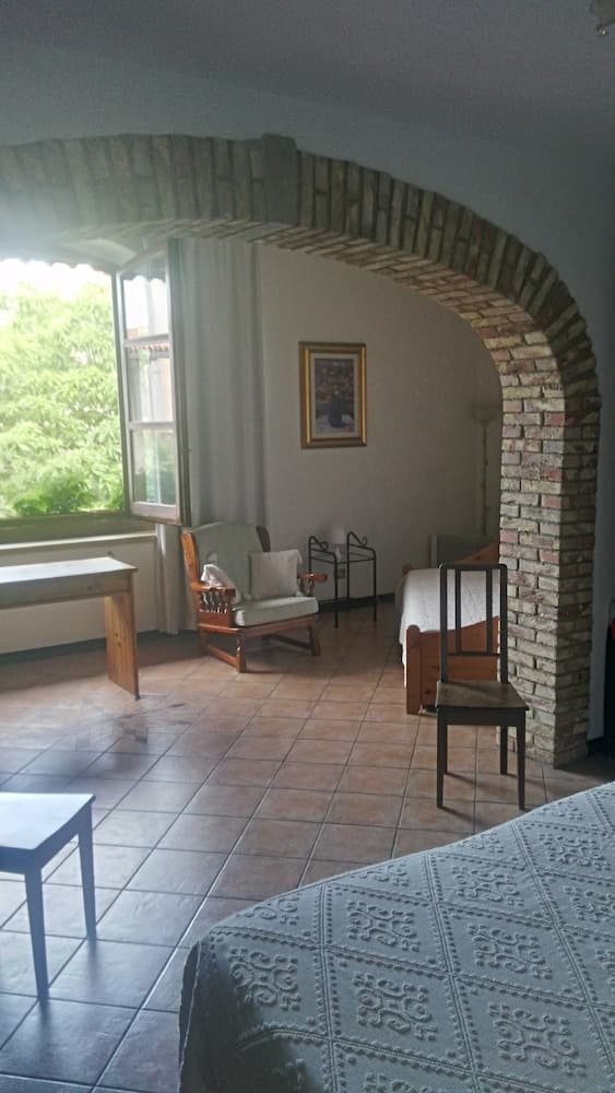A cozy bedroom with tiled floors, a brick archway, and a view of greenery through the window, ideal for travelers seeking a serene and rustic retreat.