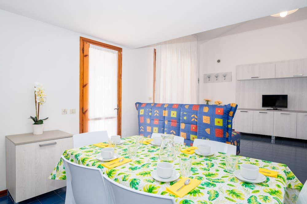 A cozy dining area with a vibrant tropical tablecloth, colorful cushioned bench, and modern kitchenette in the background, ideal for travelers seeking a bright and inviting vacation rental space.