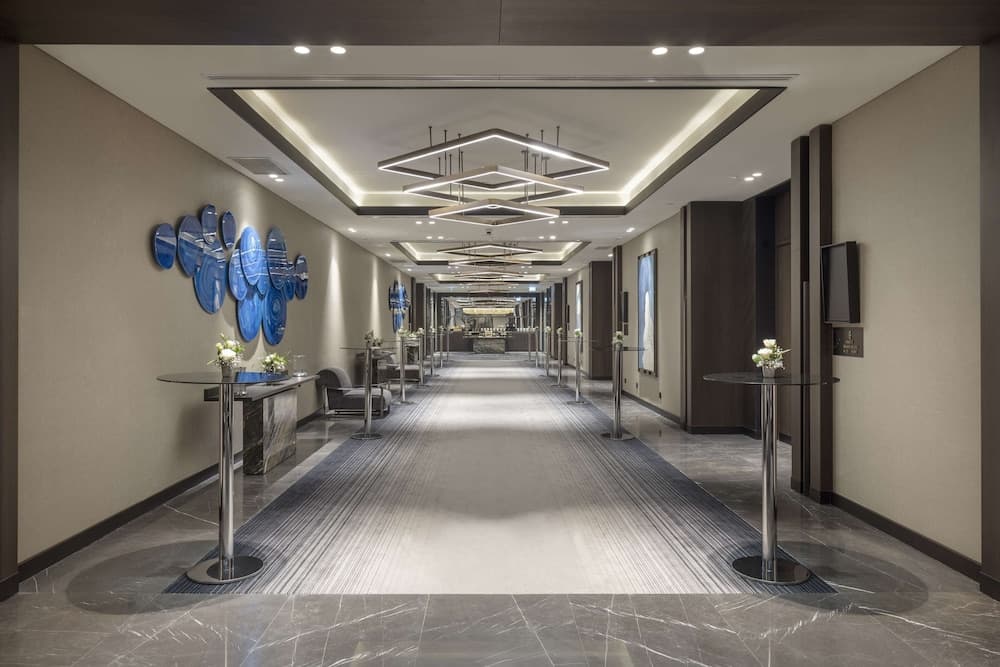 A modern hotel corridor features sleek lighting, blue circular wall art, and elegant furnishings, creating an inviting atmosphere ideal for business travelers seeking a sophisticated stay.