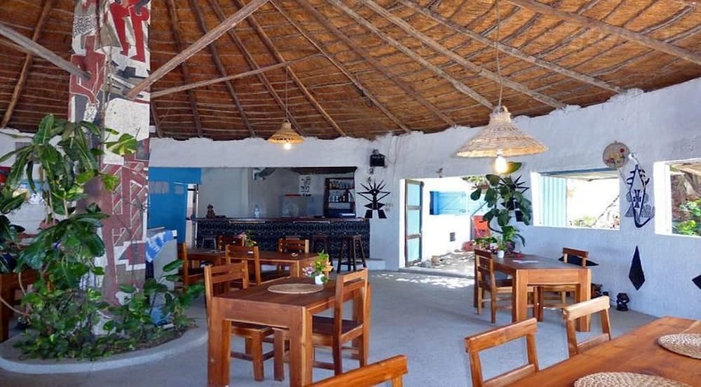 A cozy tropical café with wooden tables, thatched roof, vibrant plants, and cultural wall art offers a serene dining experience ideal for travelers seeking local charm.