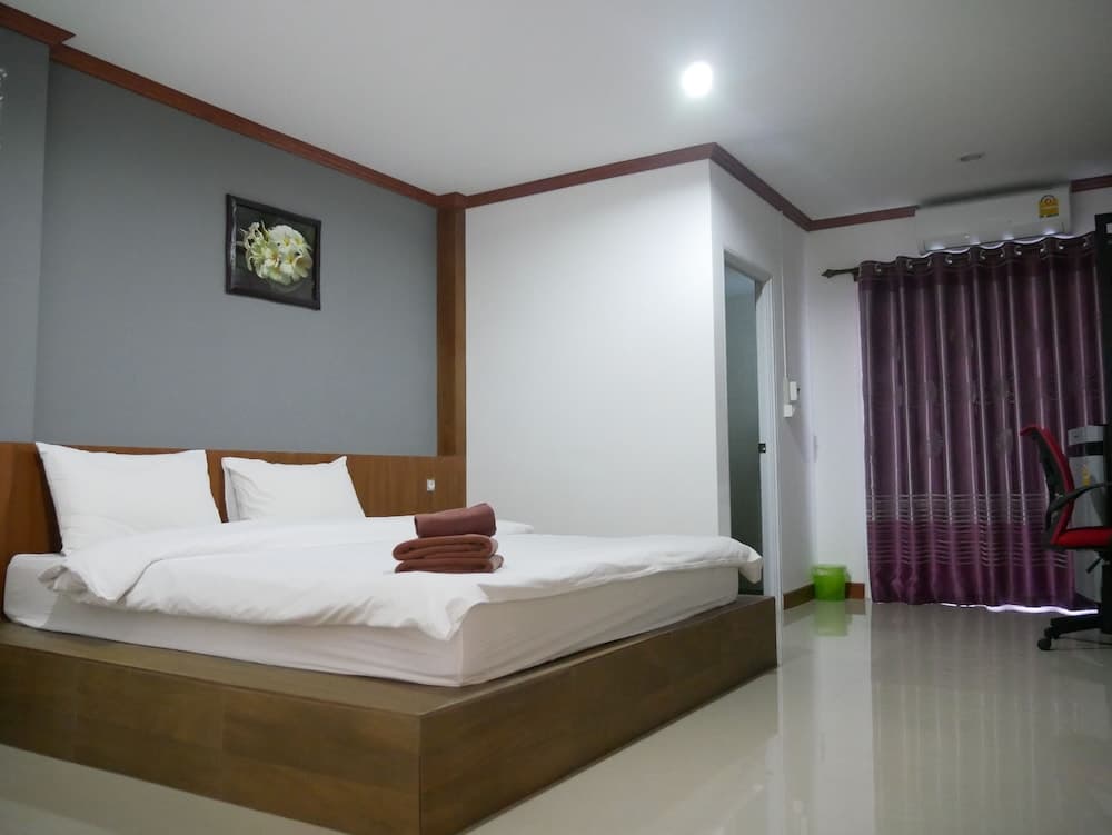 A cozy hotel room features a neatly made bed with white linens, purple curtains, and minimal decor, ideal for travelers seeking comfort and simplicity.