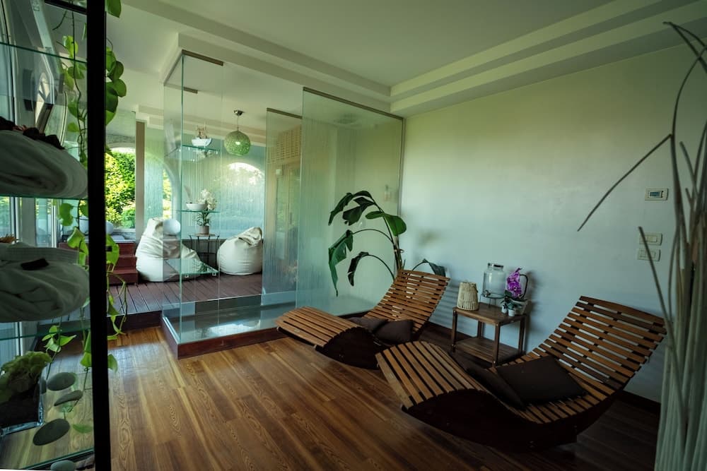 A serene indoor relaxation area features wooden loungers, lush greenery, and glass partitions, creating a tranquil atmosphere ideal for spa retreats and wellness getaways.