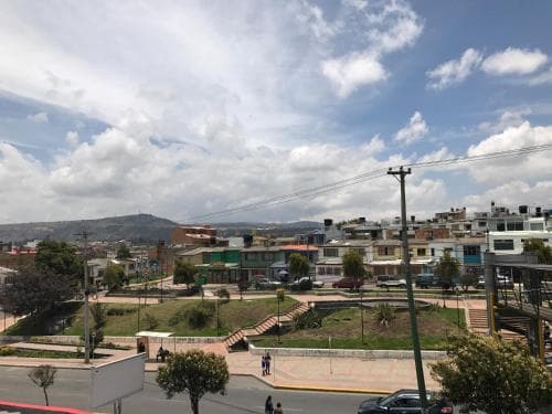 A vibrant urban plaza surrounded by colorful buildings under a partly cloudy sky offers a serene spot for travelers to relax and explore local culture.