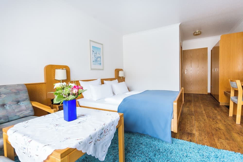 A cozy hotel room with wooden furnishings, a neatly made bed adorned with a blue blanket, a vibrant floral arrangement on a lace-covered table, and a warm, inviting atmosphere perfect for travelers seeking comfort and relaxation.