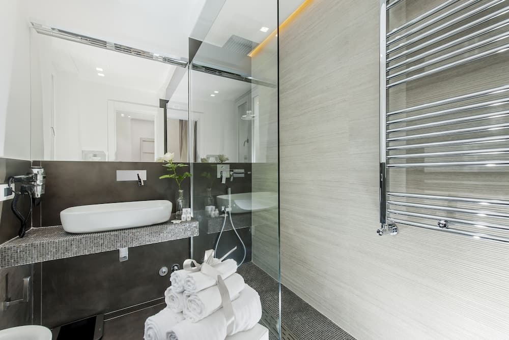 A modern, minimalist hotel bathroom features sleek surfaces, a glass-enclosed shower, neatly folded towels, and a stylish sink area, ideal for travelers seeking comfort and elegance.