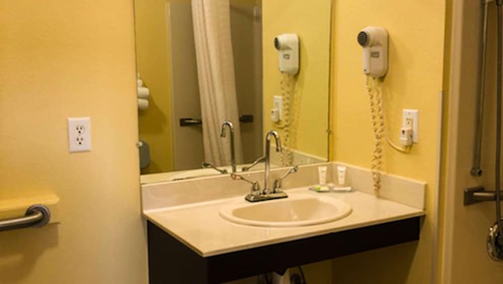 A cozy hotel bathroom features a sink with a large mirror, yellow walls, a mounted hairdryer, and accessible amenities, ideal for travelers seeking comfort and convenience.