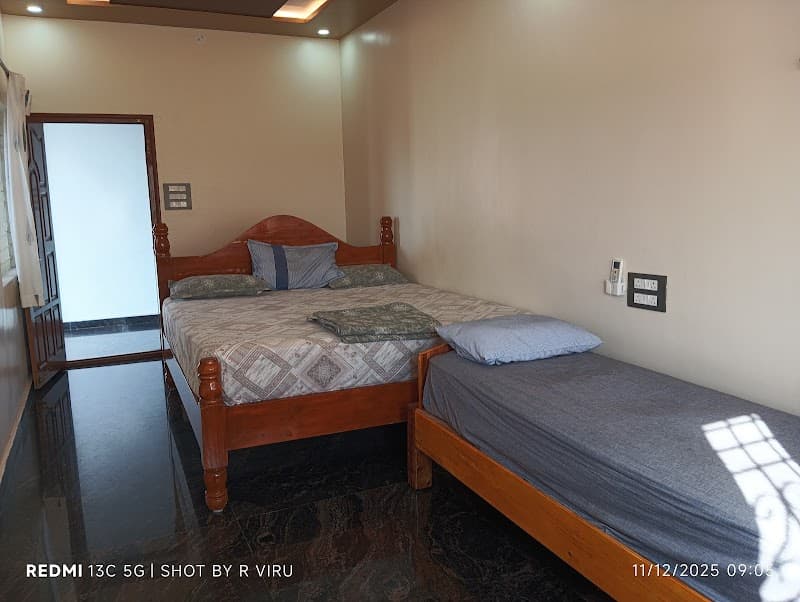 A cozy bedroom at Lakshmi Villa Hampi features wooden beds, soft lighting, and a serene ambiance, ideal for travelers seeking comfort in Karnataka's historic region.