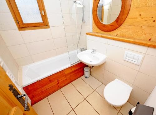 A cozy bathroom with tiled floors, wooden accents, and a bathtub-shower combo offers a functional and inviting space for travelers seeking comfort in their accommodations.