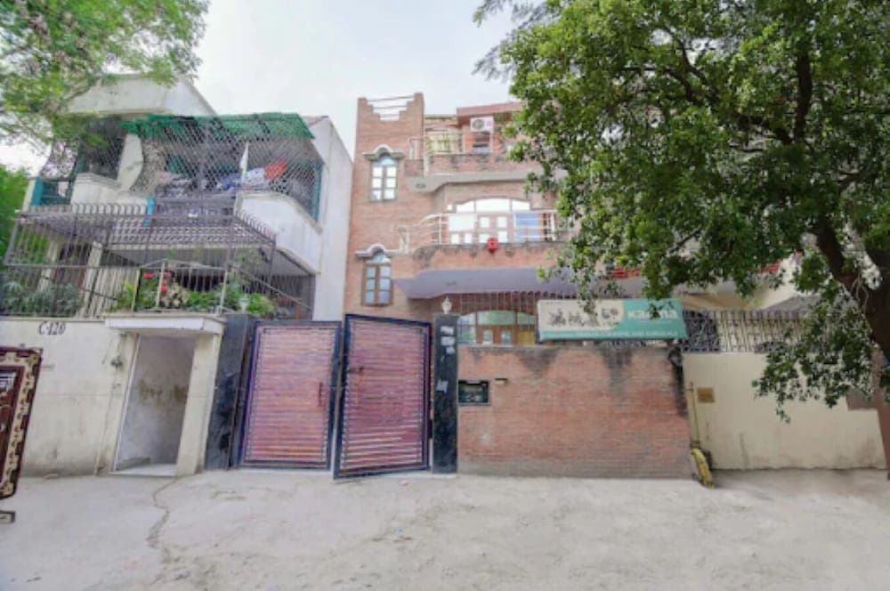 A serene residential street features a gated property with a brick wall, lush green trees, and multi-story buildings, ideal for travelers seeking a quiet urban retreat.