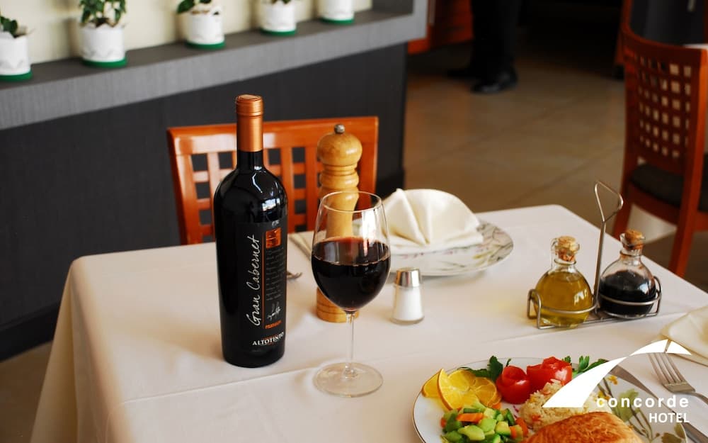 A cozy restaurant table set with a bottle of Gran Cabernet wine, a glass, a colorful salad, and condiments, inviting travelers to enjoy a fine dining experience in a warm and elegant atmosphere.