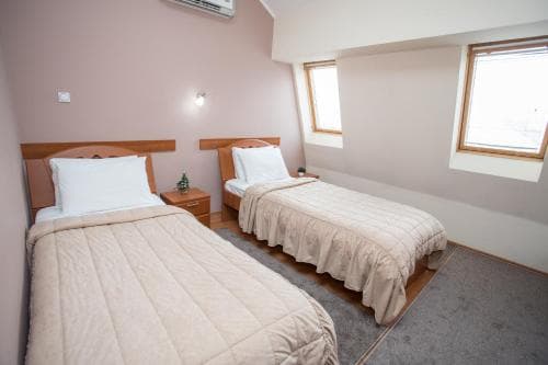 A cozy attic bedroom with two neatly made beds under slanted ceilings, featuring soft lighting and small windows, ideal for travelers seeking a quiet and intimate accommodation experience.