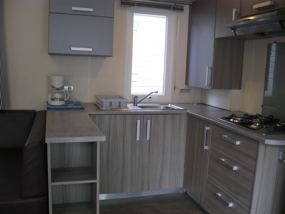 A cozy, modern kitchenette with sleek wooden cabinets, a stainless steel sink, and a coffee maker by the window, ideal for travelers seeking a compact yet functional space in a vacation rental.