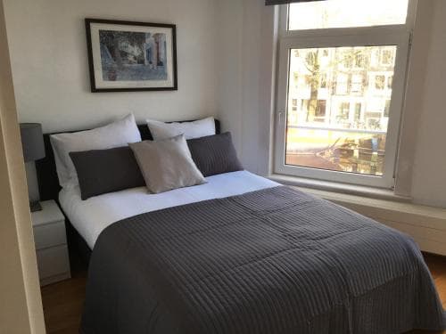 A cozy hotel room with a neatly made bed, soft lighting, and a window view of urban scenery offers a serene retreat for travelers seeking comfort and relaxation.