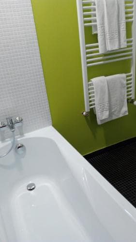 A modern bathroom with a sleek white bathtub, vibrant green wall, and neatly arranged towels on a heated towel rack creates a clean and inviting atmosphere, ideal for travelers seeking comfort and relaxation.