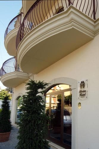 A charming hotel entrance with elegant balconies and lush greenery invites travelers seeking a cozy stay in a serene urban setting.