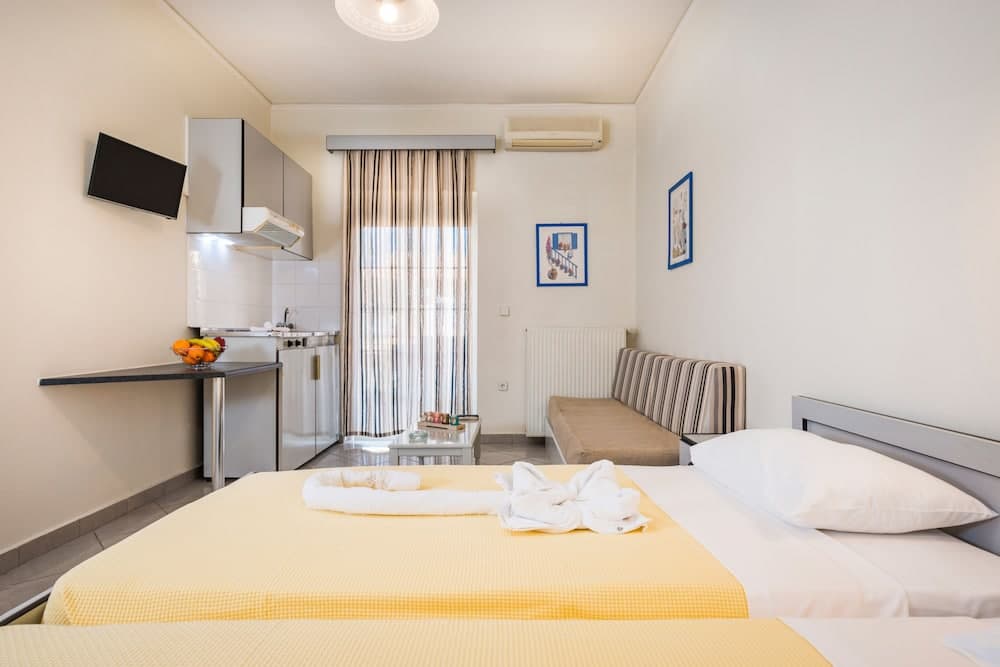 A cozy studio apartment features a neatly made bed with yellow bedding, a small kitchenette, and a comfortable seating area, ideal for travelers seeking a compact yet functional living space.