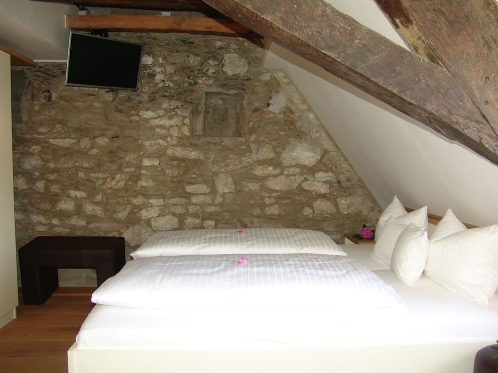 A cozy attic bedroom with exposed wooden beams, a rustic stone wall, and neatly arranged bedding offers a charming retreat for travelers seeking a unique and intimate stay.
