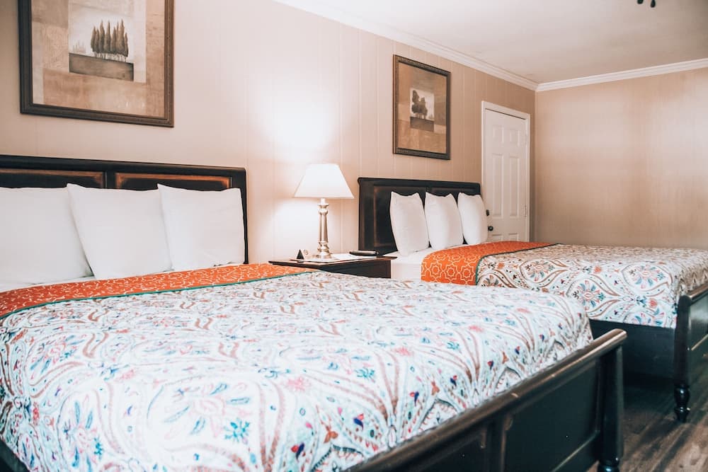 A cozy hotel room features two neatly made beds with vibrant paisley-patterned bedding, framed artwork on the walls, and a warm ambiance ideal for travelers seeking comfort and relaxation.