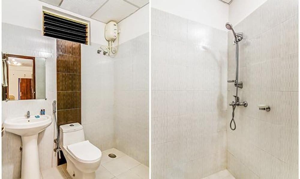 A clean and functional bathroom with white tiled walls, a shower area, toilet, sink, mirror, and wall-mounted heater, ideal for travelers seeking basic yet comfortable accommodations.