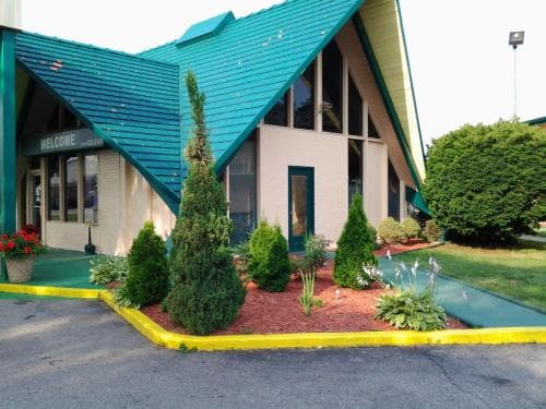A cozy motel entrance with a vibrant green roof and welcoming landscaping invites travelers seeking a comfortable stay in a serene suburban setting.