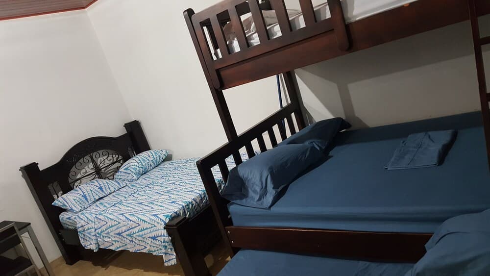 A cozy hostel room features a bunk bed with blue bedding and a single bed with patterned sheets, ideal for budget travelers seeking comfortable accommodations.