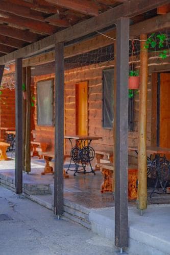 A cozy log cabin porch with rustic wooden tables and chairs invites travelers to relax in a serene, countryside setting ideal for a peaceful getaway.