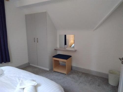 A cozy attic bedroom with slanted ceilings features a neatly made bed, a wardrobe, a small vanity with a mirror, and soft lighting, ideal for travelers seeking a quiet and intimate accommodation experience.