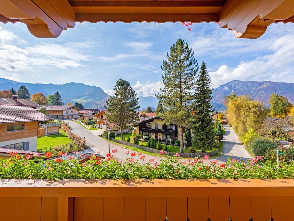 A serene balcony view captures a picturesque village nestled among lush greenery and towering mountains, ideal for travelers seeking a tranquil retreat in nature.