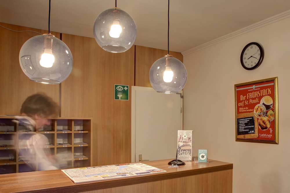 A cozy reception area with wooden shelves, spherical pendant lights, and a breakfast advertisement creates a welcoming atmosphere ideal for travelers seeking local information and services.