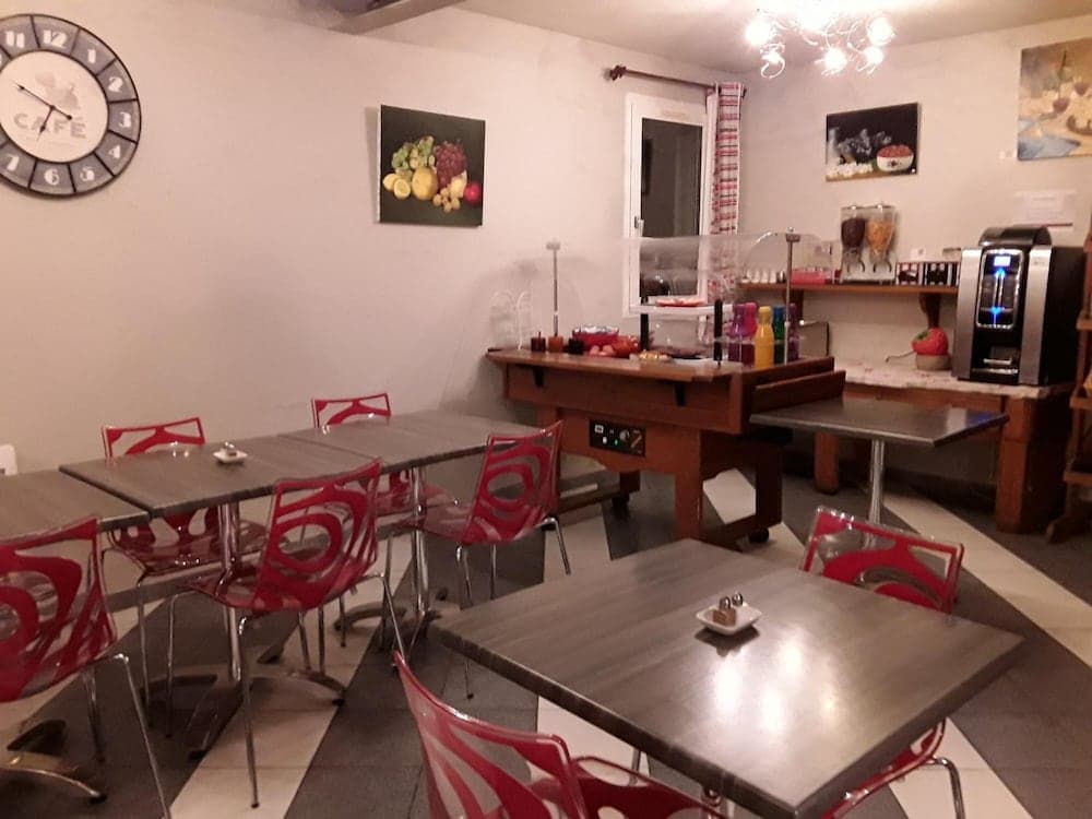 A cozy café interior features modern red chairs around sleek tables, a fruit-themed wall art, and a coffee machine, ideal for travelers seeking a quiet spot to relax and enjoy refreshments.