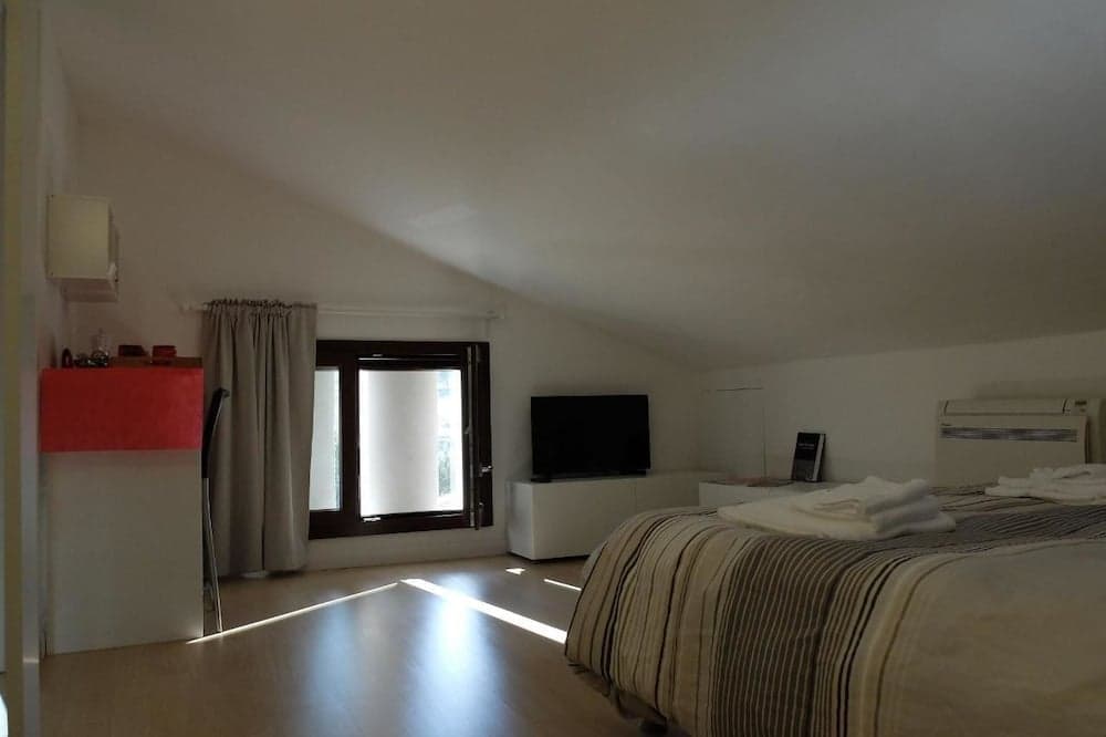 A cozy attic bedroom with sloped ceilings features a neatly made bed, a flat-screen TV, and soft natural light streaming through a window, ideal for travelers seeking a serene and comfortable retreat.