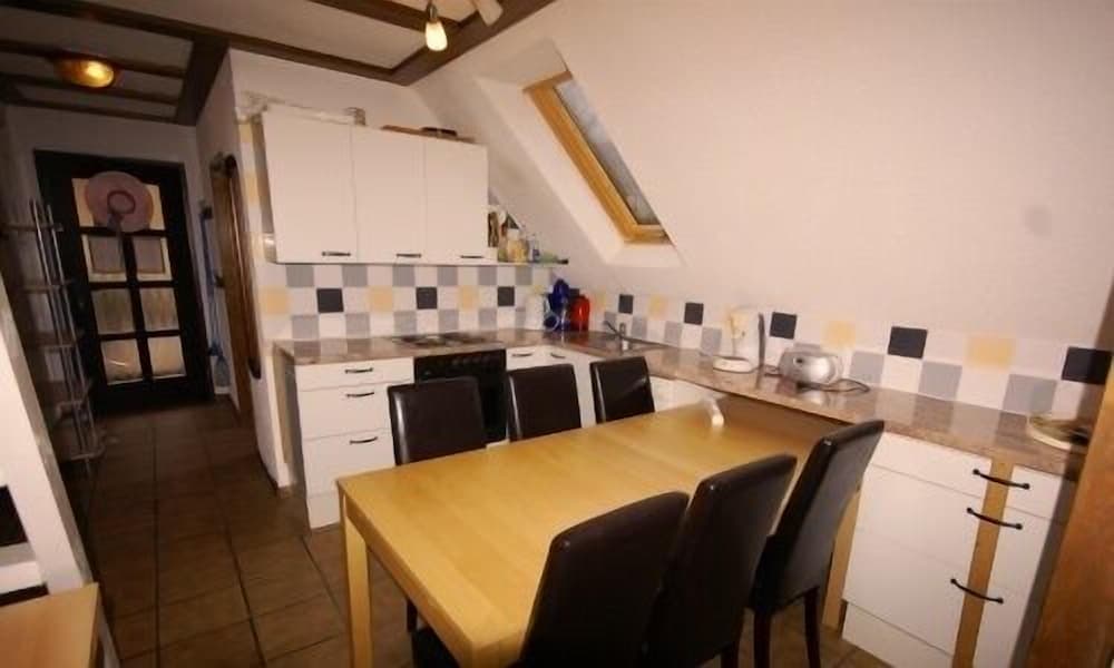 A cozy attic kitchen with white cabinets, a checkered backsplash, and a wooden dining table creates a warm and inviting atmosphere, perfect for travelers seeking a homey accommodation experience.