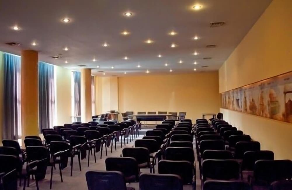 A spacious conference room with rows of chairs, warm yellow walls, and a mural, ideal for professional gatherings and presentations.