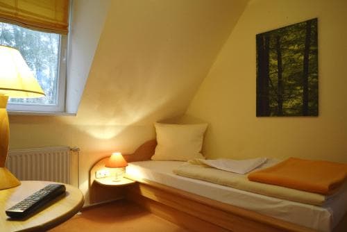 A cozy attic bedroom with sloped ceilings features a neatly made bed, warm lighting, and a forest-themed artwork, ideal for travelers seeking a tranquil and intimate accommodation experience.