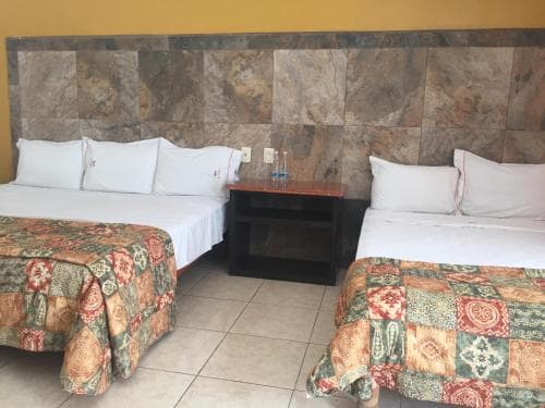 A cozy hotel room features two beds with colorful patchwork quilts against a stone-tiled wall, creating a warm and inviting atmosphere ideal for travelers seeking comfort and relaxation.