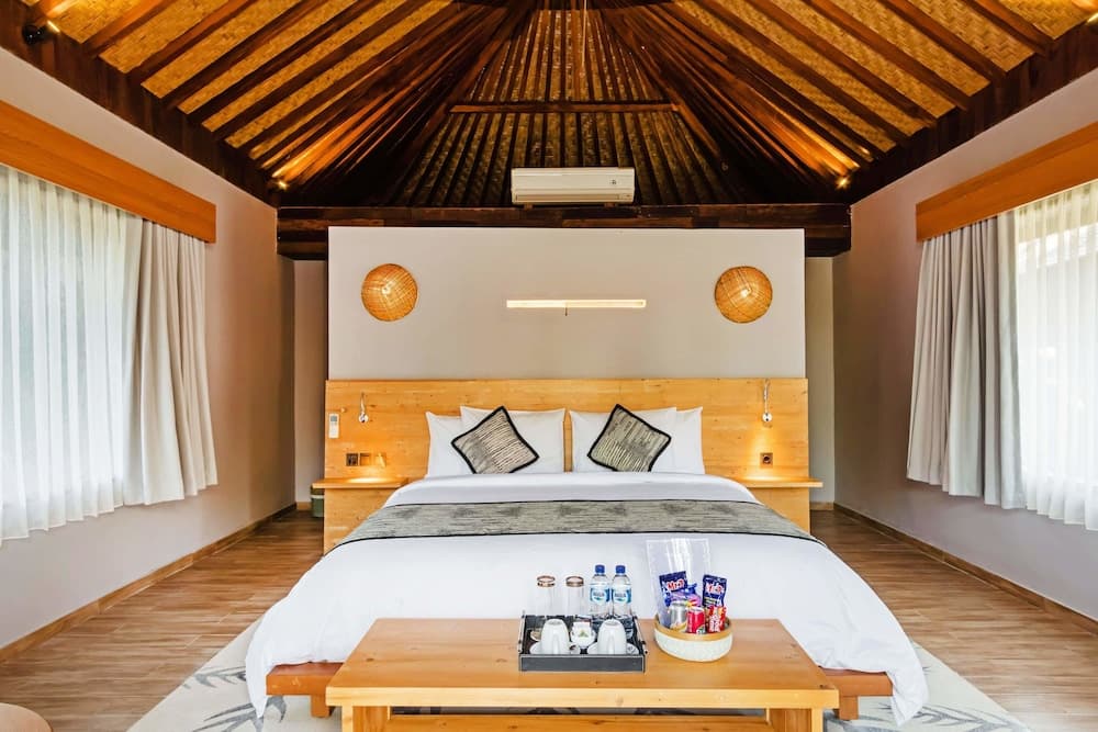 A cozy bedroom with a wooden ceiling, large bed adorned with patterned pillows, and a table offering refreshments creates an inviting atmosphere ideal for travelers seeking relaxation in a rustic retreat.