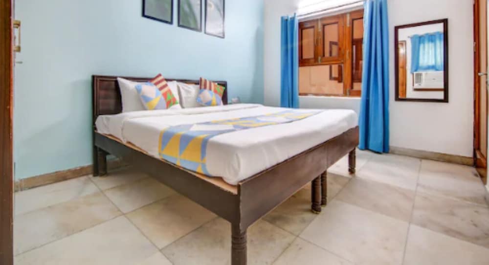 A cozy hotel room with a neatly made bed adorned in colorful linens, blue curtains framing a wooden cabinet, and framed artwork on light blue walls, ideal for travelers seeking comfort and simplicity.