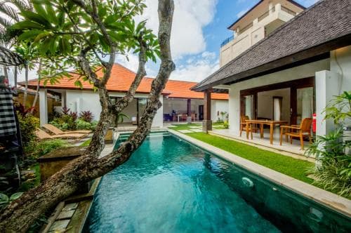 A serene tropical villa features a tranquil pool lined with lush greenery and wooden furniture, ideal for a relaxing vacation getaway.