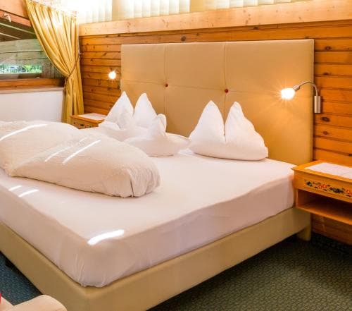 A cozy hotel room with wooden paneling, neatly arranged pillows on a plush bed, warm lighting, and a bedside table, ideal for travelers seeking comfort and relaxation.
