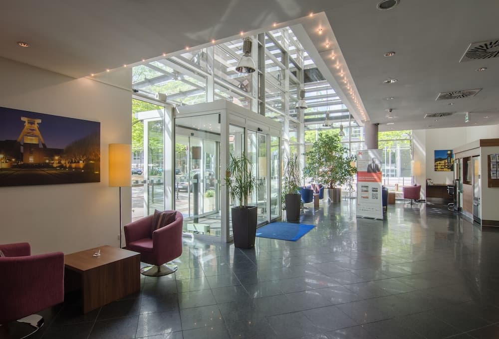 A modern hotel lobby with sleek tiled floors, vibrant seating areas, large glass windows letting in natural light, and indoor plants creates a welcoming atmosphere ideal for travelers seeking comfort and style.