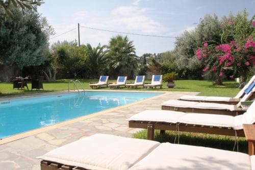 A serene outdoor poolside scene with lounge chairs, lush greenery, blooming flowers, and palm trees, ideal for relaxing vacations in a tranquil resort setting.
