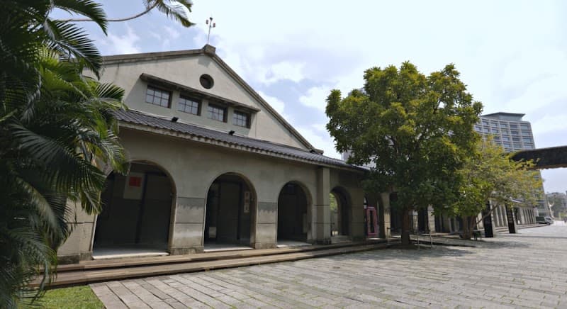 A serene courtyard at the Songshan Cultural and Creative Park No 1. Warehouse in Taipei's Xinyi District showcases historic architecture with arched doorways, lush greenery, and a tranquil ambiance, ideal for cultural exploration and photography enthusiasts.