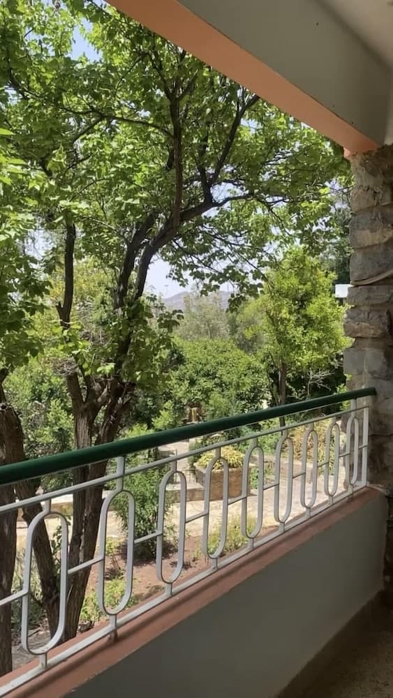 A serene balcony view framed by lush green trees and a stone pillar, perfect for travelers seeking a tranquil retreat in nature.