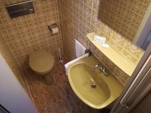 A cozy hotel bathroom features a yellow sink and toilet against patterned wallpaper, creating a warm and inviting atmosphere ideal for travelers seeking comfort during their stay.