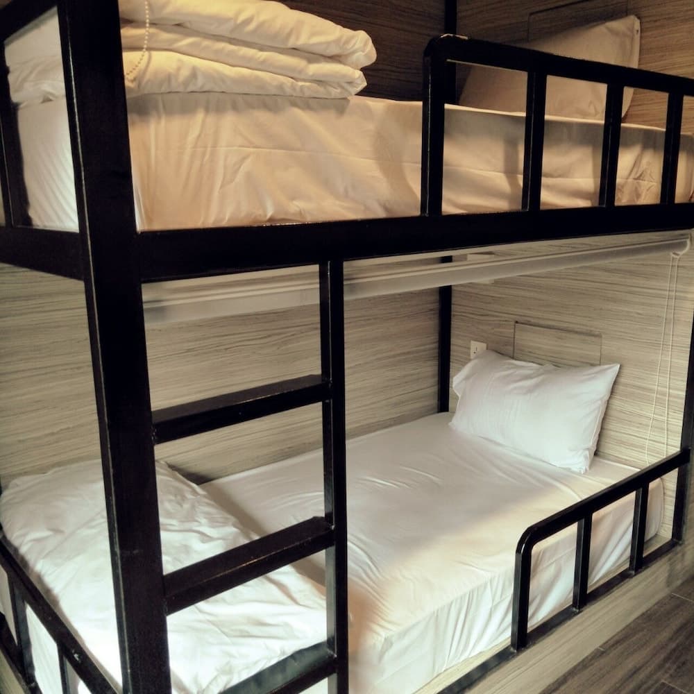 A cozy hostel room features neatly made bunk beds with white linens against a wood-paneled wall, ideal for budget travelers seeking comfortable accommodations.
