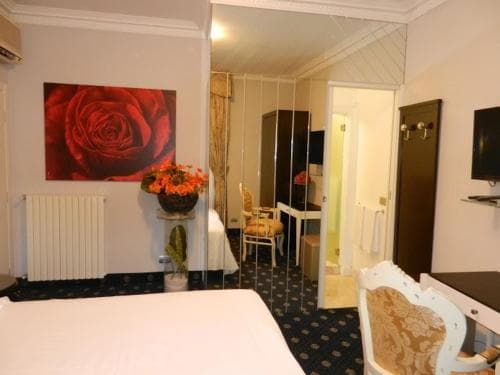 A cozy hotel room features a vibrant red rose artwork, patterned carpet, and a small dining area, creating an inviting atmosphere ideal for travelers seeking comfort and convenience.