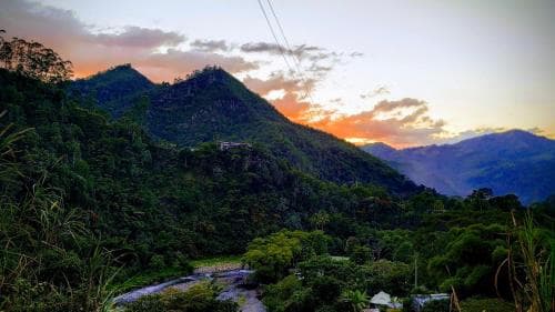 A serene sunset bathes lush green mountains in warm hues, creating an ideal backdrop for tranquil hiking adventures amidst nature's splendor.