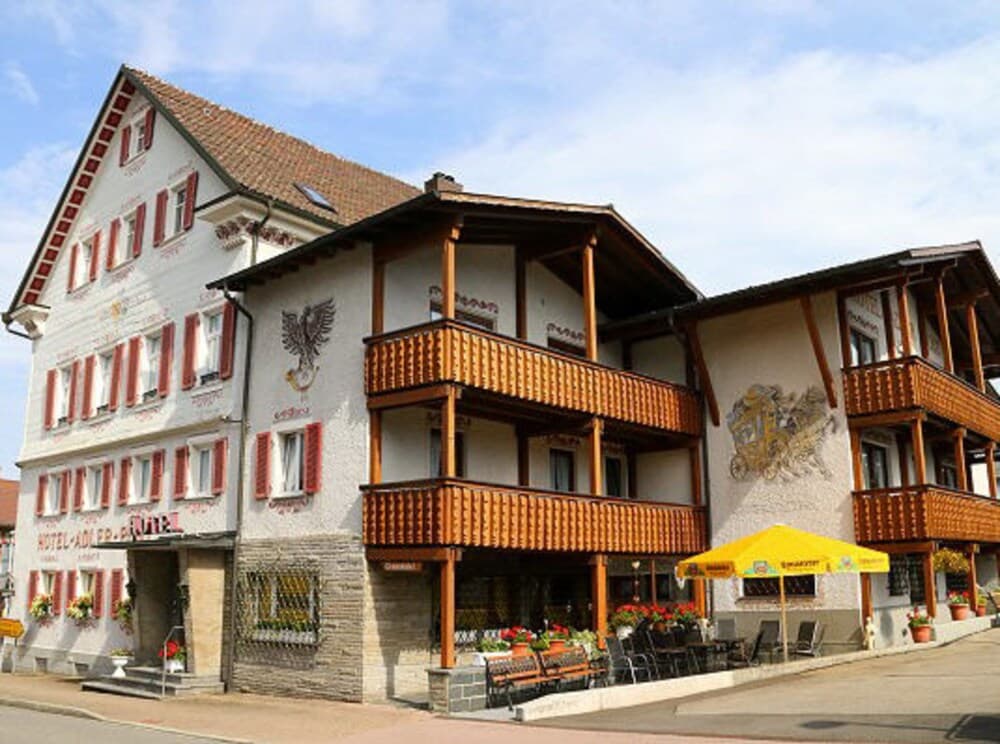A charming European hotel with wooden balconies and vibrant flower arrangements invites travelers to enjoy its cozy outdoor seating under a sunny sky, perfect for a relaxing getaway.