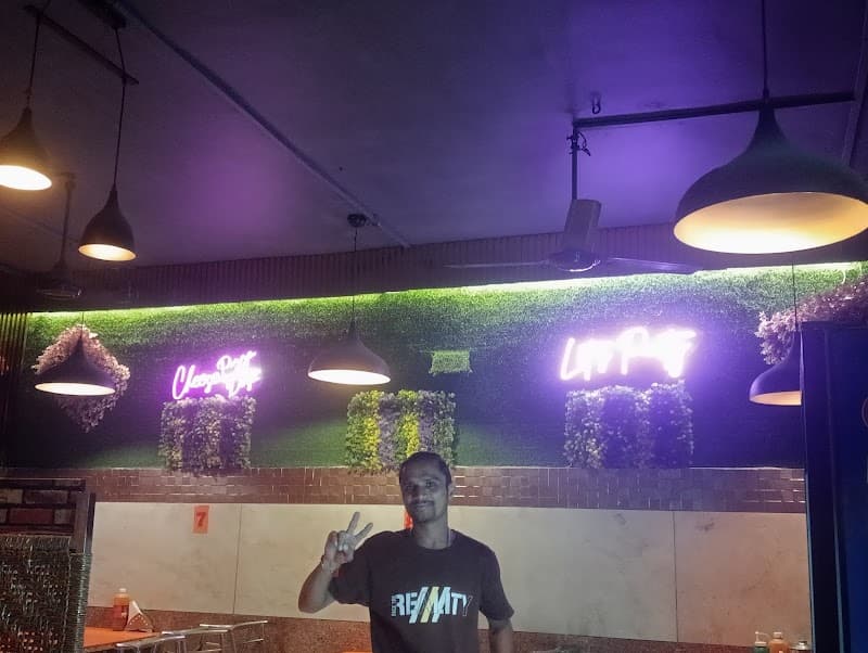 A cozy indoor dining area at Vineet Restaurant in Meerut, Uttar Pradesh, features vibrant neon signs, greenery-adorned walls, and warm lighting, creating an inviting atmosphere perfect for travelers seeking local cuisine.